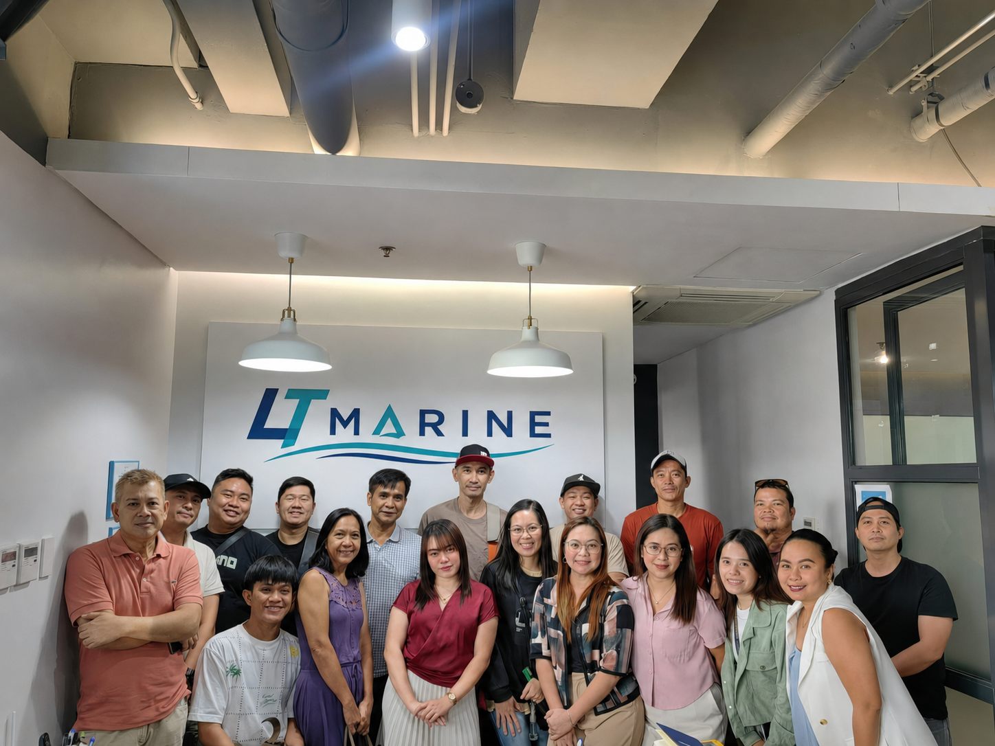 A large group photo of LT Marine seafarers together with the shore and office team in front of the company logo wall.